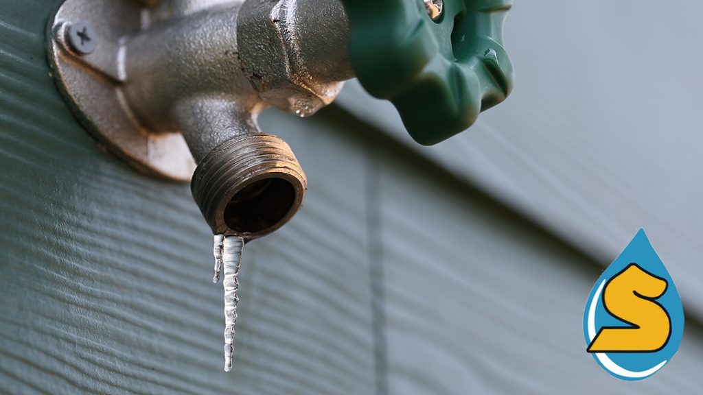 A frozen winter faucet on the side of a home with ice dripping from the open nozzle
