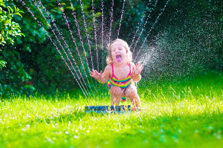Child playing with garden sprinkler. Kid in bathing suit running and jumping. Kids gardening. Summer outdoor water fun. Children play with gardening hose watering flowers.